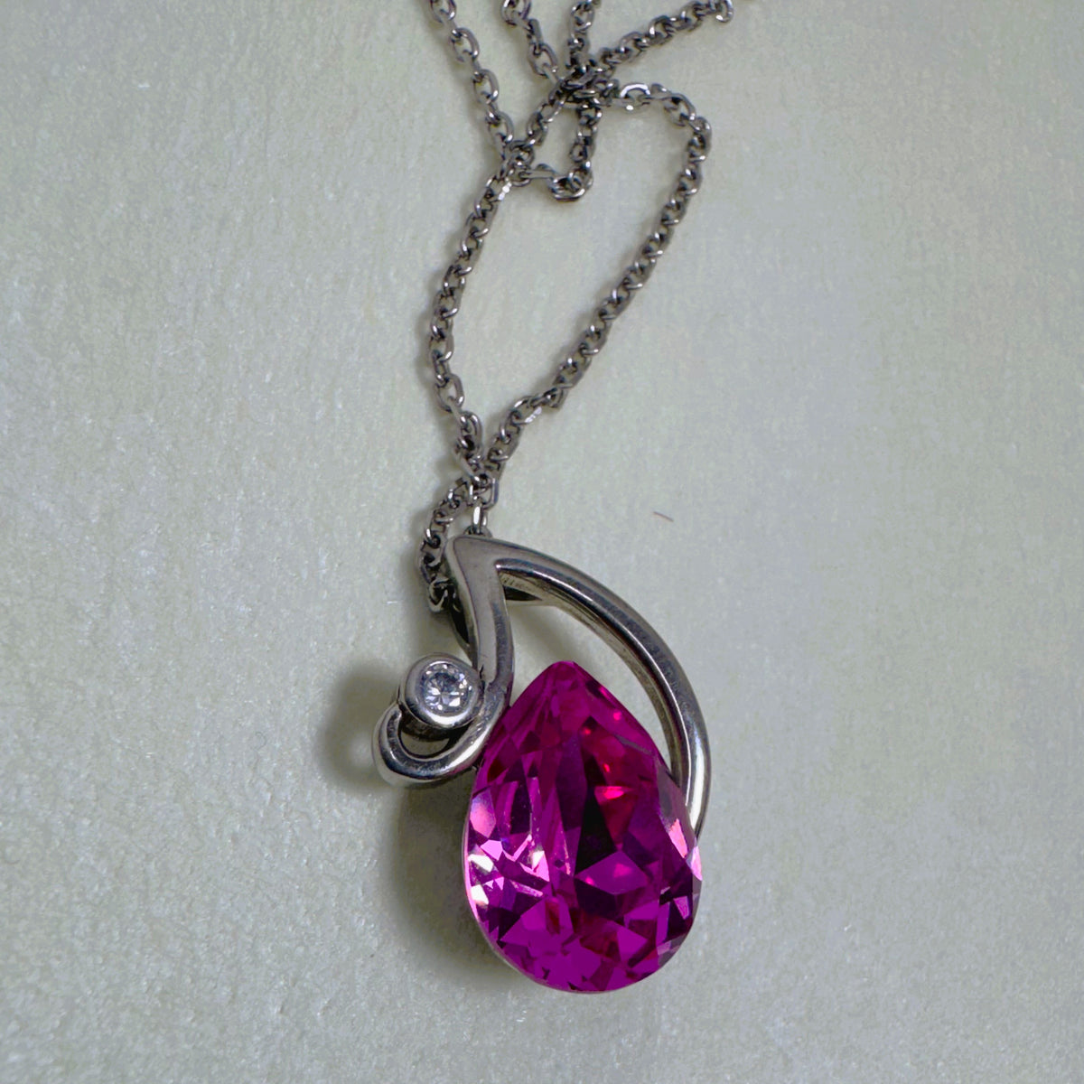 Sterling silver pendant necklace with a large pink pear cut glass stone in a swirl setting, on a cable chain.