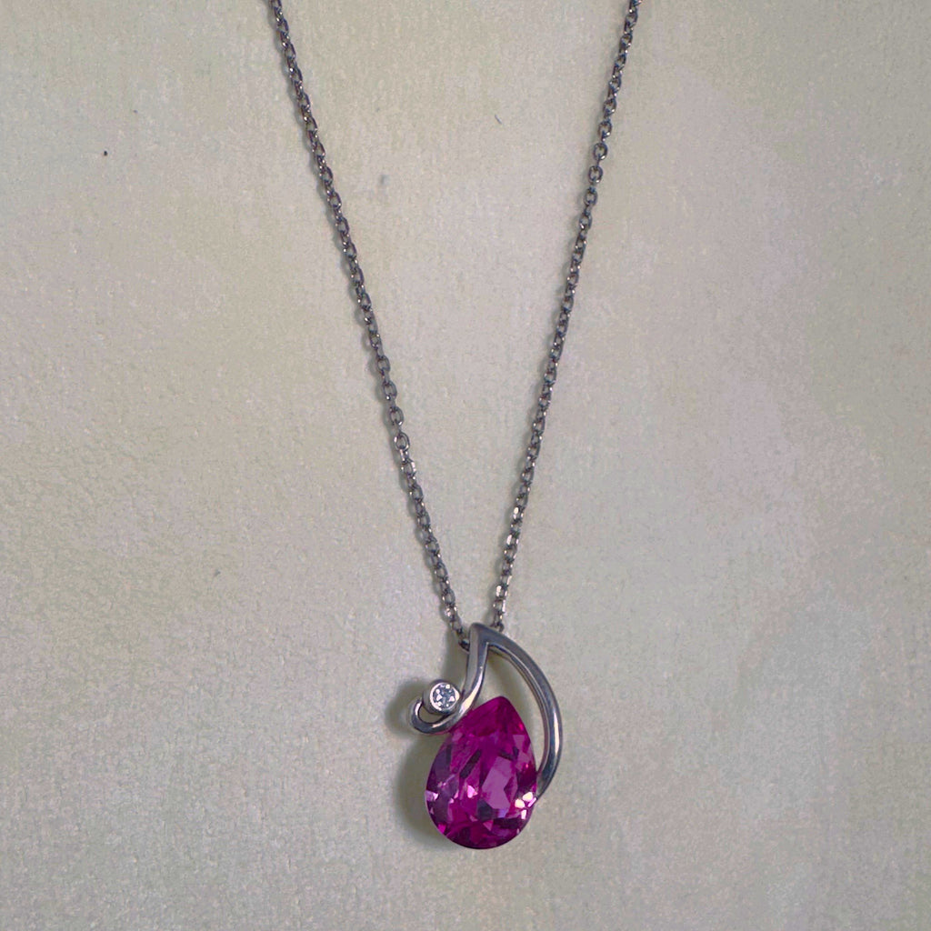 The pendant necklace laid out on a pale surface with the chain above.