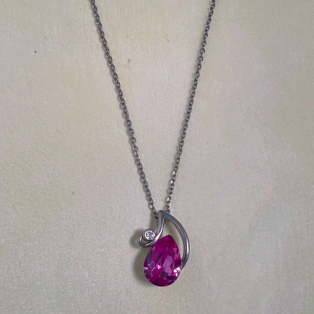 The pendant necklace laid out on a pale surface with the chain above.