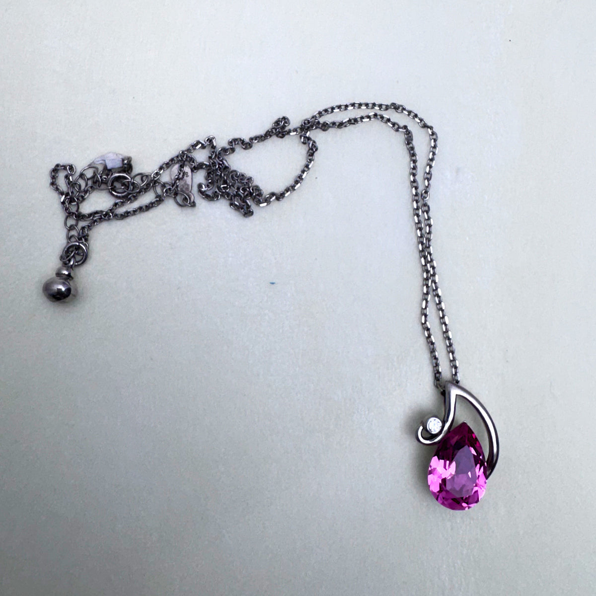 The full necklace laid out with the extender chain and the pink stone pendant.