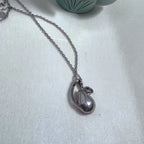 The plain silver back of the swirl pendant on the chain.