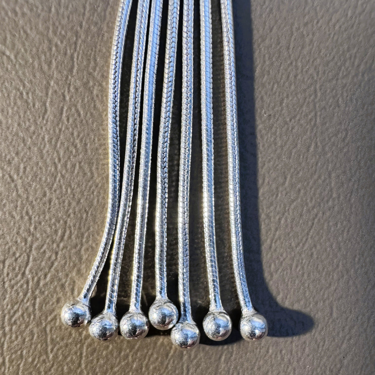 Close view of the snake chain strands of the tassel, each ending in a silver ball.