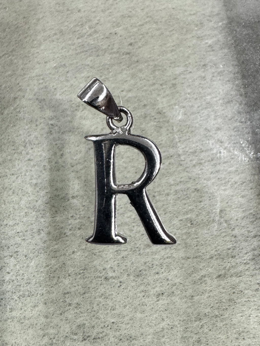 Polished sterling silver initial R pendant with a tapered bail, lying on pale grey felt.