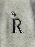 Polished sterling silver initial R pendant with a tapered bail, lying on pale grey felt.