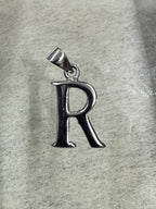 Polished sterling silver initial R pendant with a tapered bail, lying on pale grey felt.