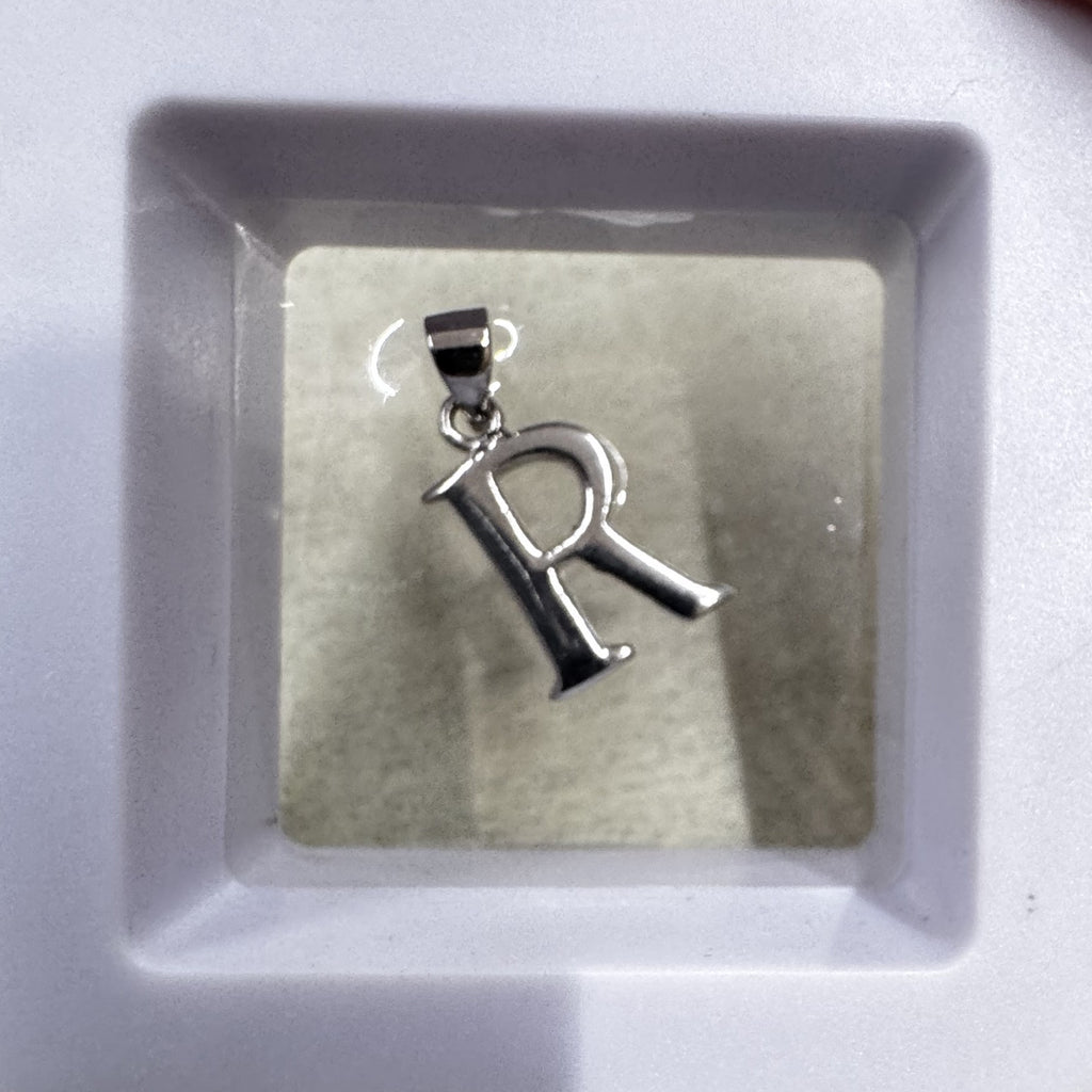 Sterling silver initial R pendant shown upright in a white ceramic dish, bail at the top.