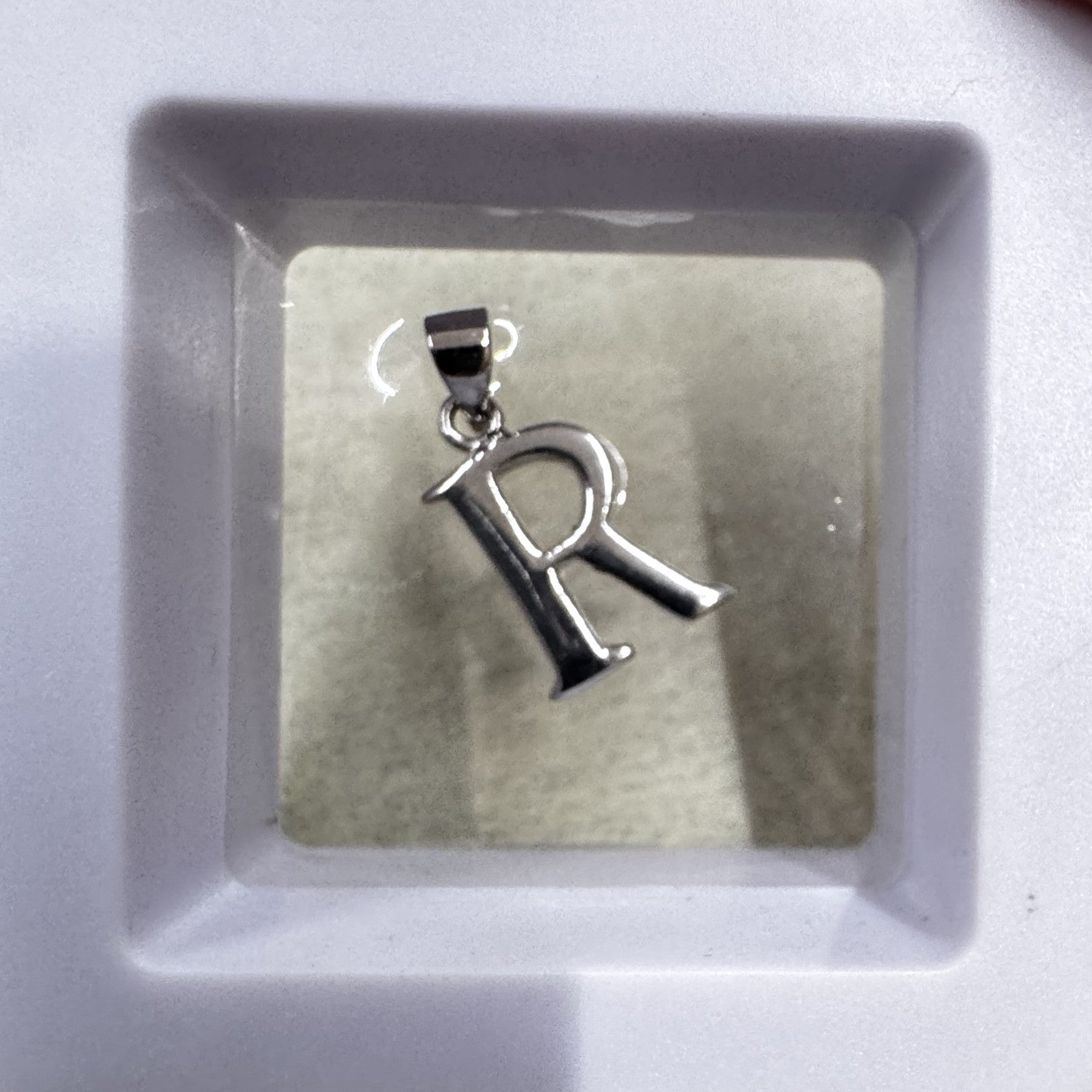 Sterling silver initial R pendant shown upright in a white ceramic dish, bail at the top.