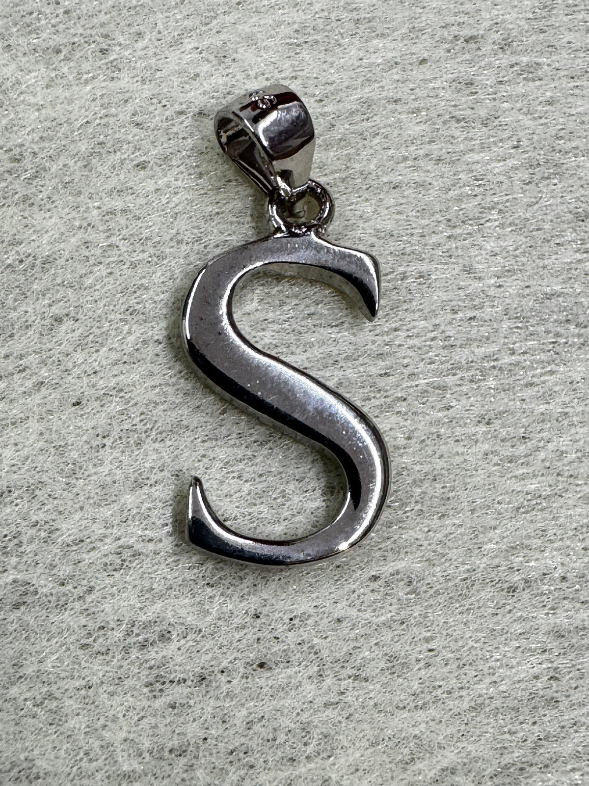 Polished sterling silver initial S pendant with hooked terminals, resting on pale grey felt.