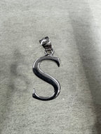 Side-lit view of the sterling silver initial S pendant and its tapered bail on grey felt.