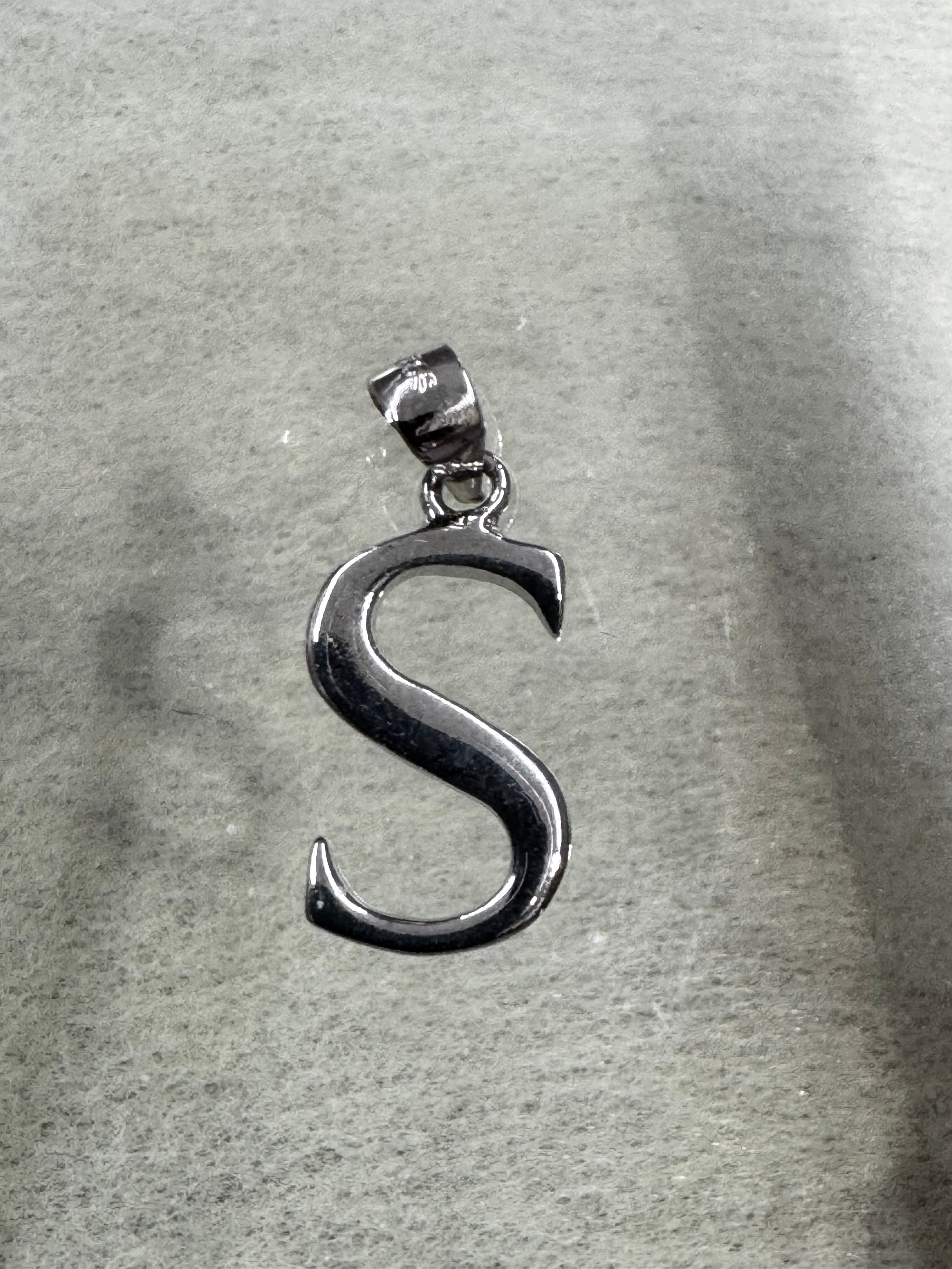 Side-lit view of the sterling silver initial S pendant and its tapered bail on grey felt.
