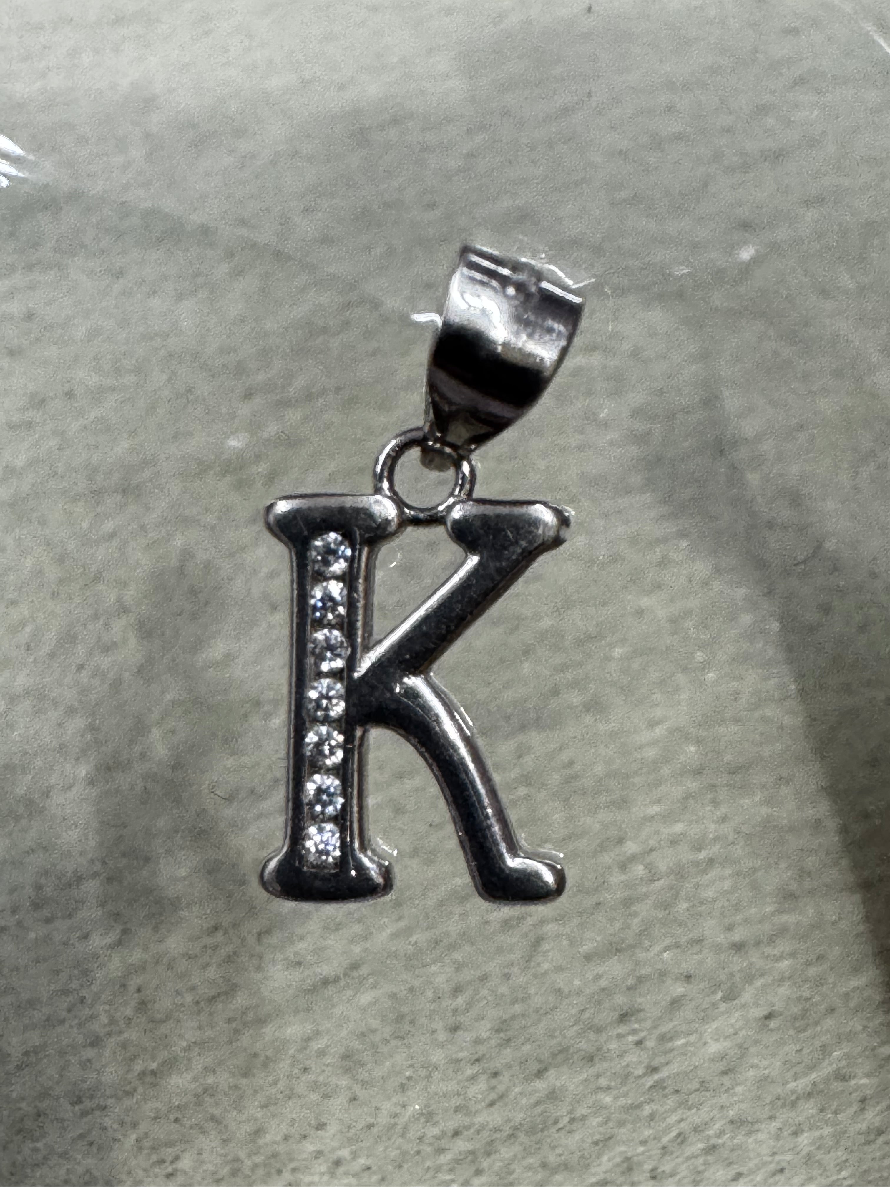 Sterling silver initial K pendant with a row of channel-set cubic zirconia, on pale grey felt.