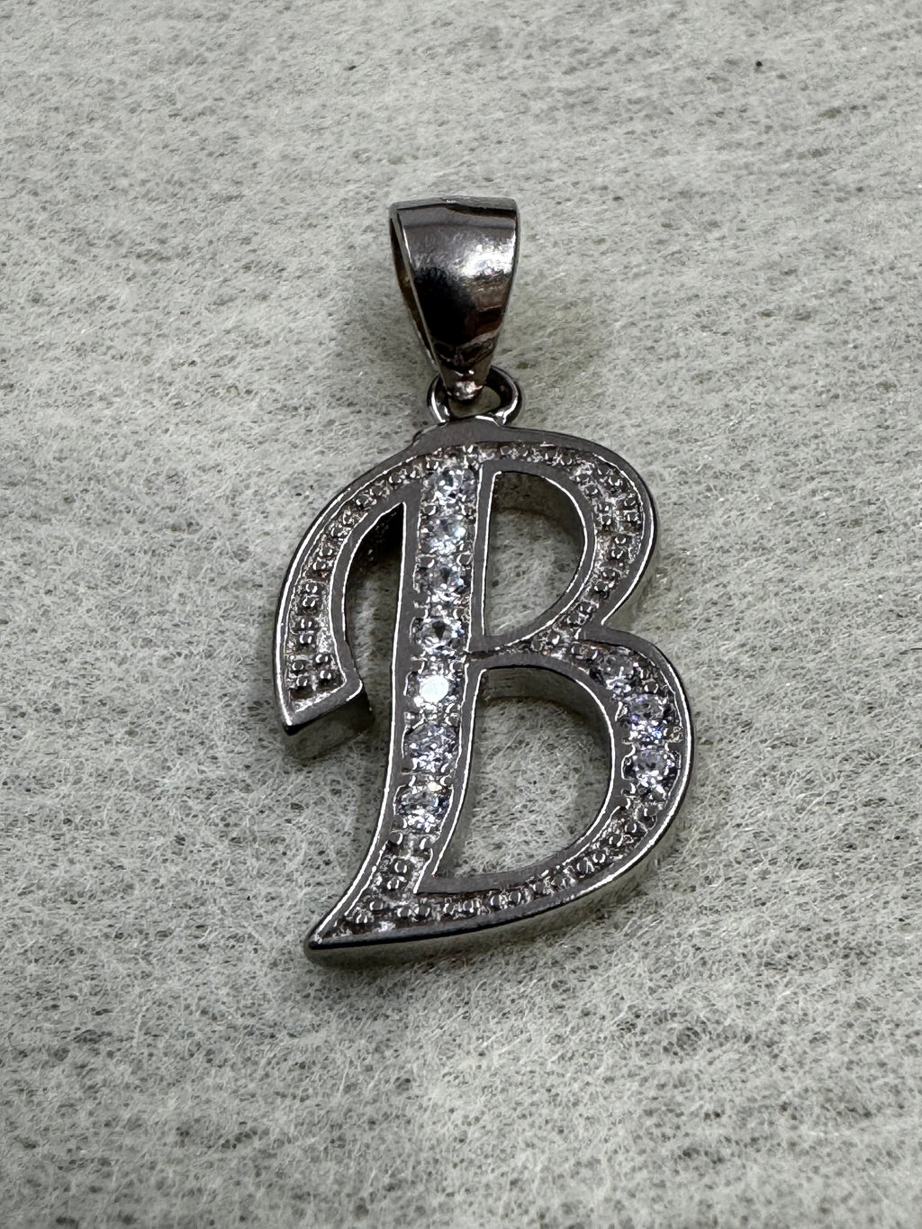 Sterling silver script initial B pendant with cubic zirconia pavé-set along its open strokes, on grey felt.