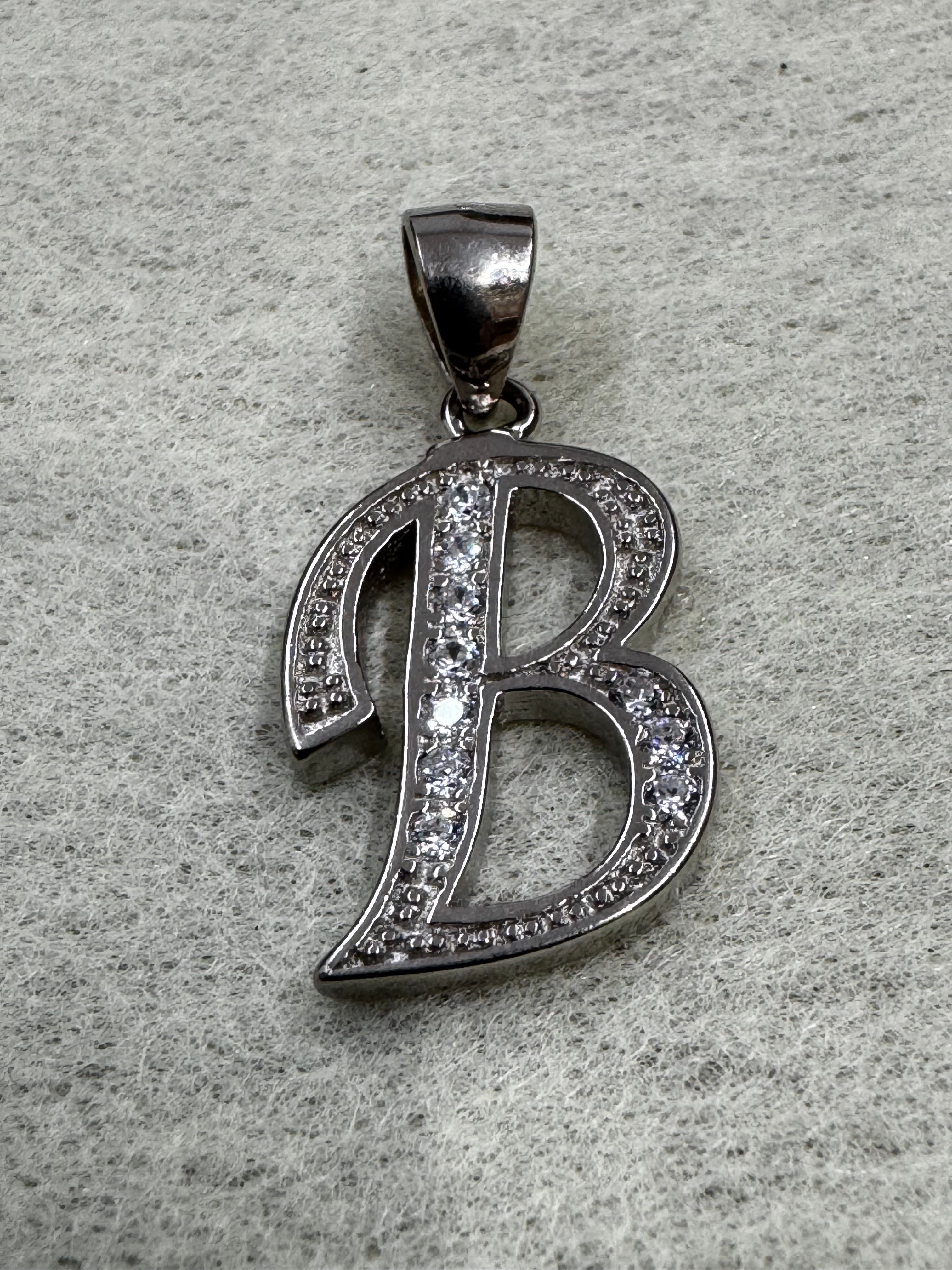 Sterling silver script initial B pendant with cubic zirconia pavé-set along its open strokes, on grey felt.