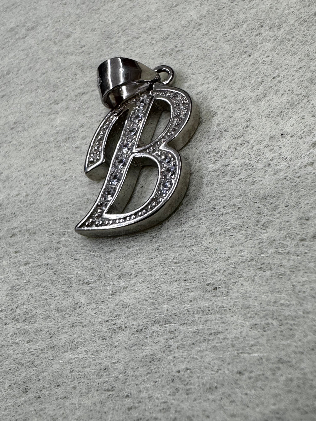Angled view of the sterling silver initial B pendant with its tapered bail folded to one side.