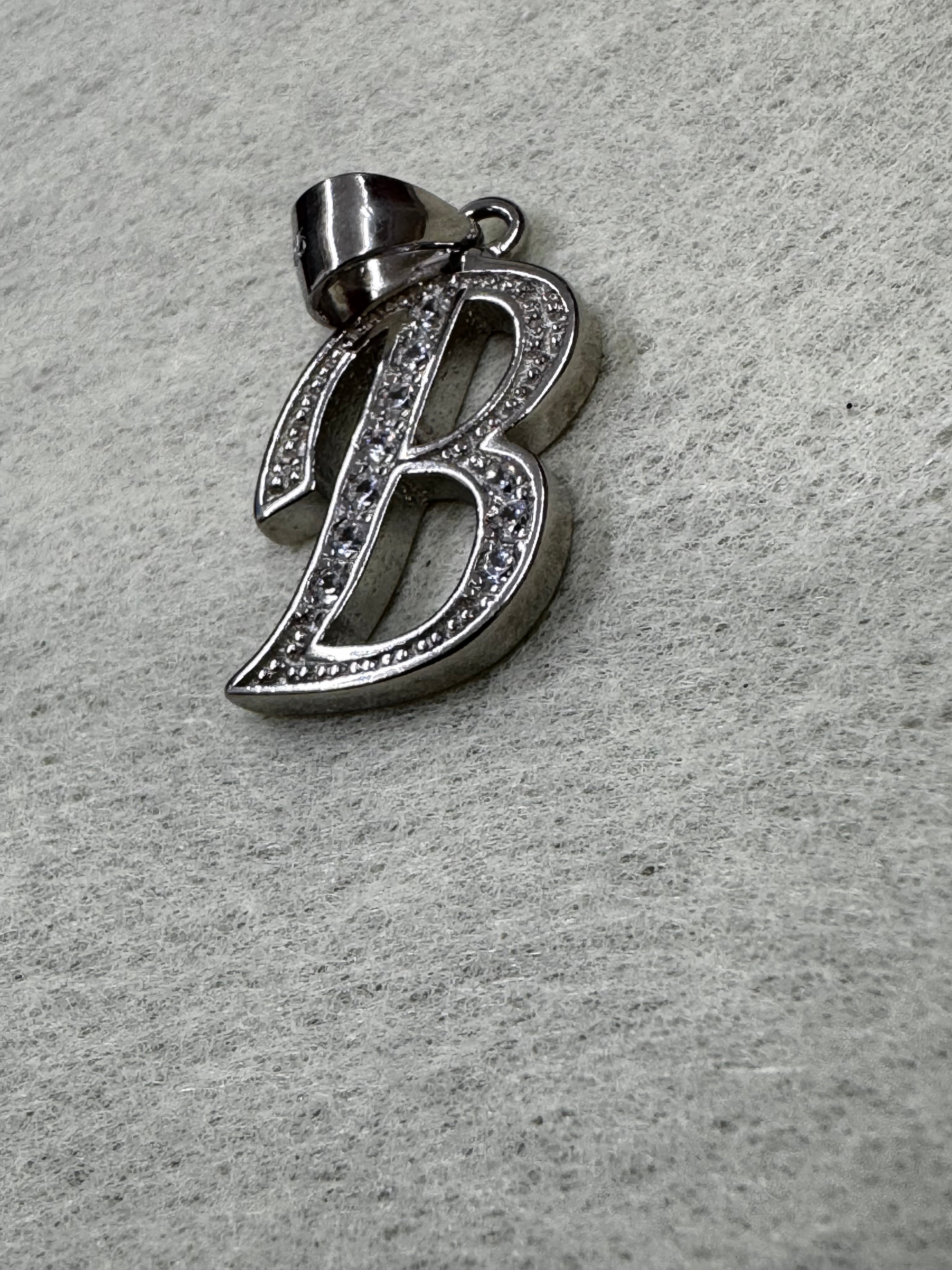 Angled view of the sterling silver initial B pendant with its tapered bail folded to one side.