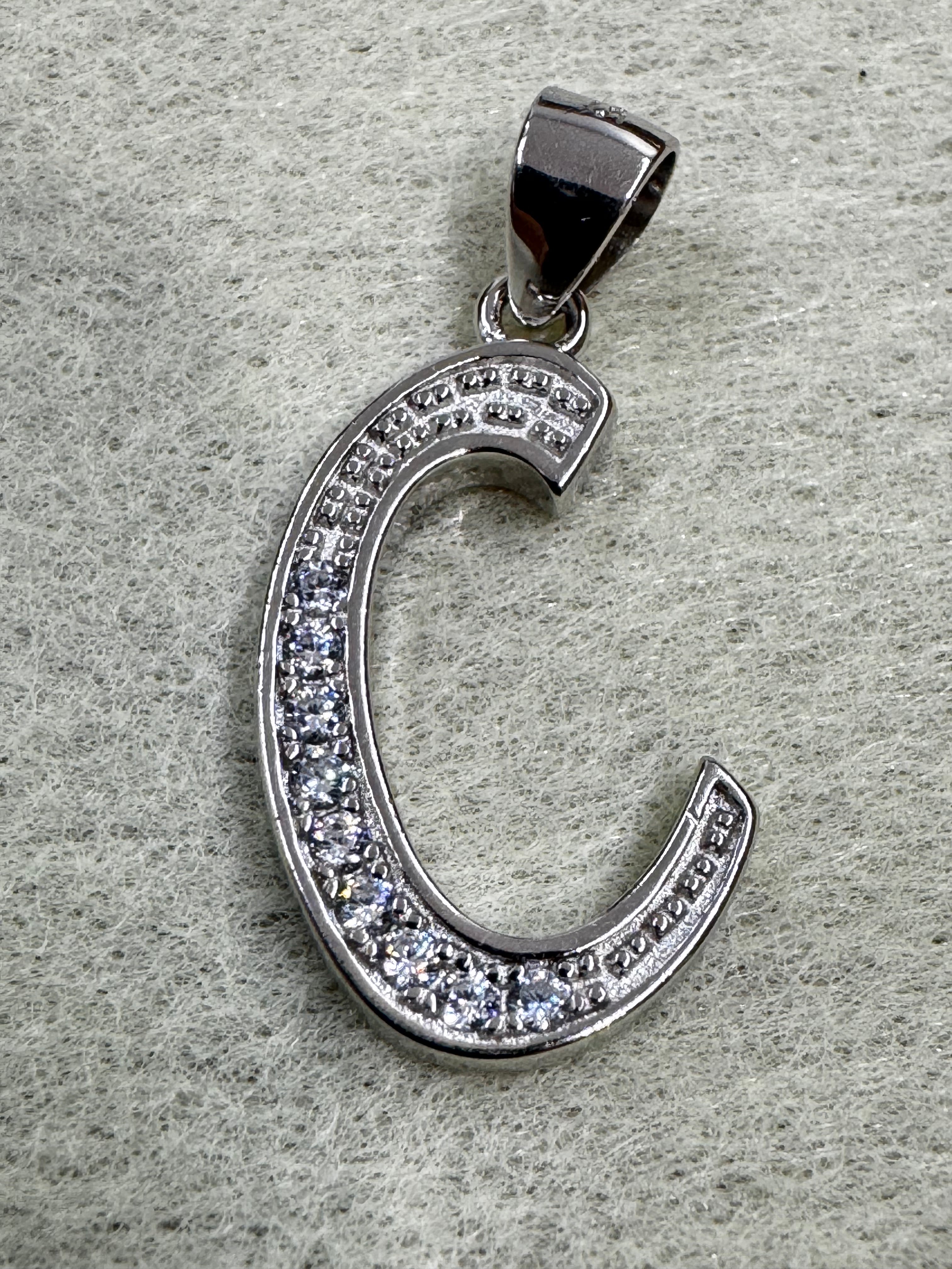 Sterling silver script initial C pendant with cubic zirconia pavé along the curve, on grey felt.