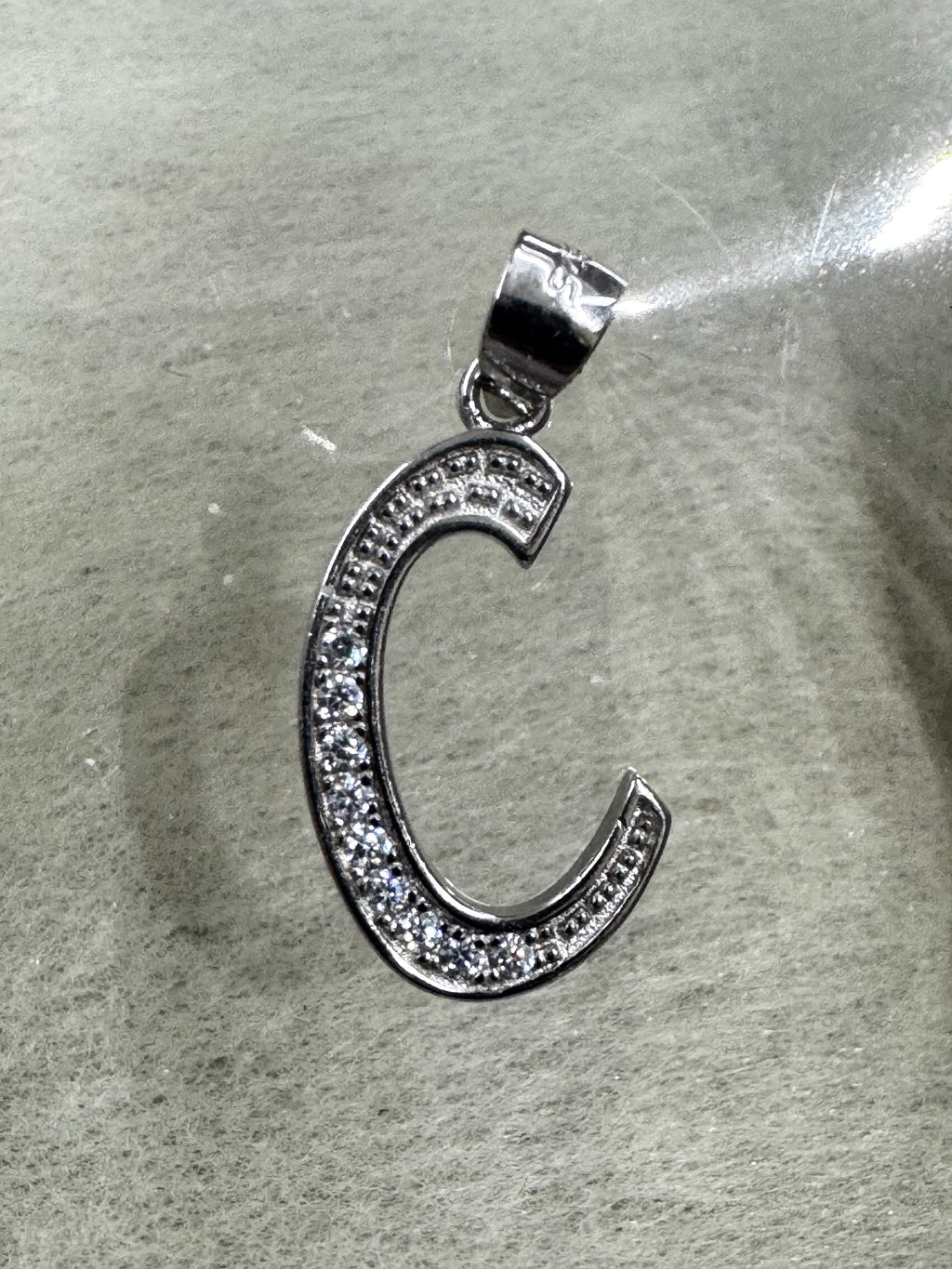 Side-lit view of the sterling silver initial C pendant and its polished tapered bail.