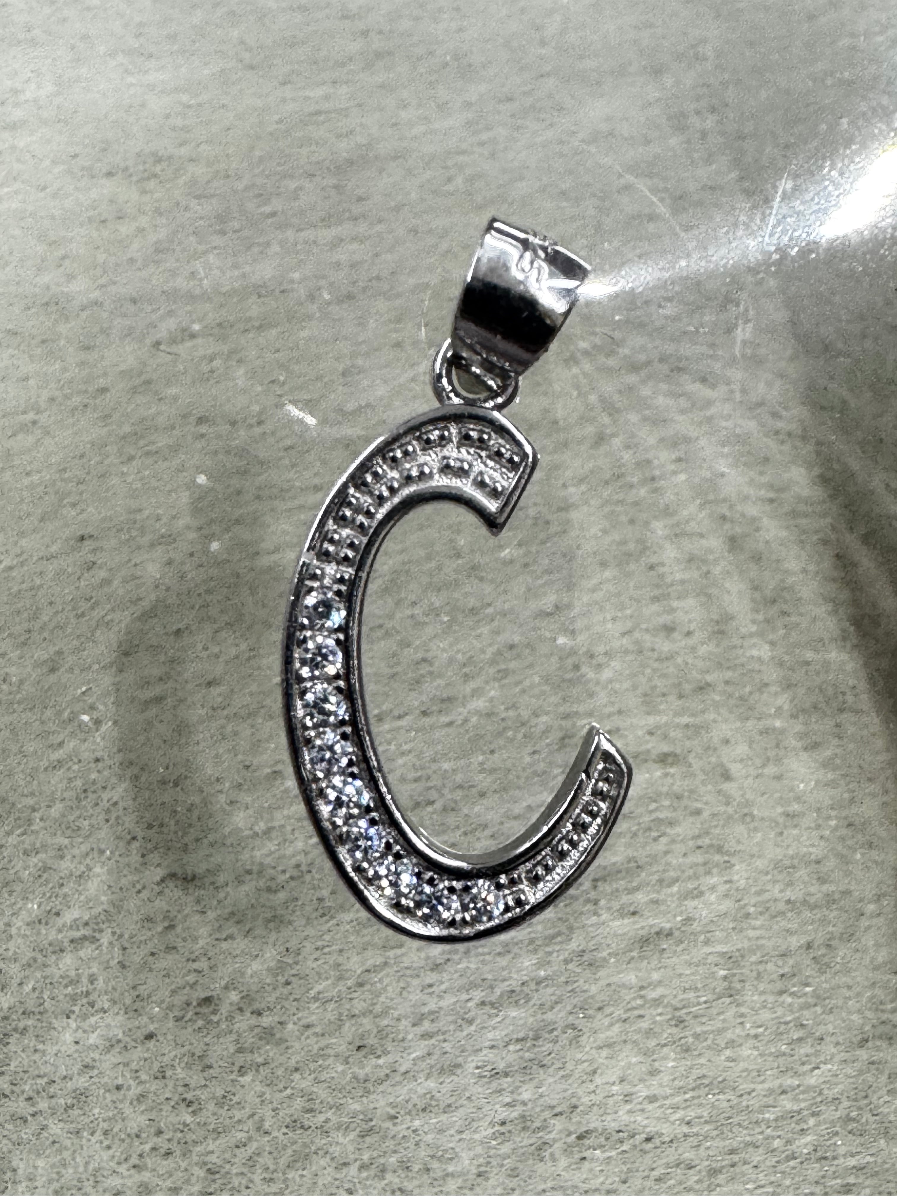 Side-lit view of the sterling silver initial C pendant and its polished tapered bail.
