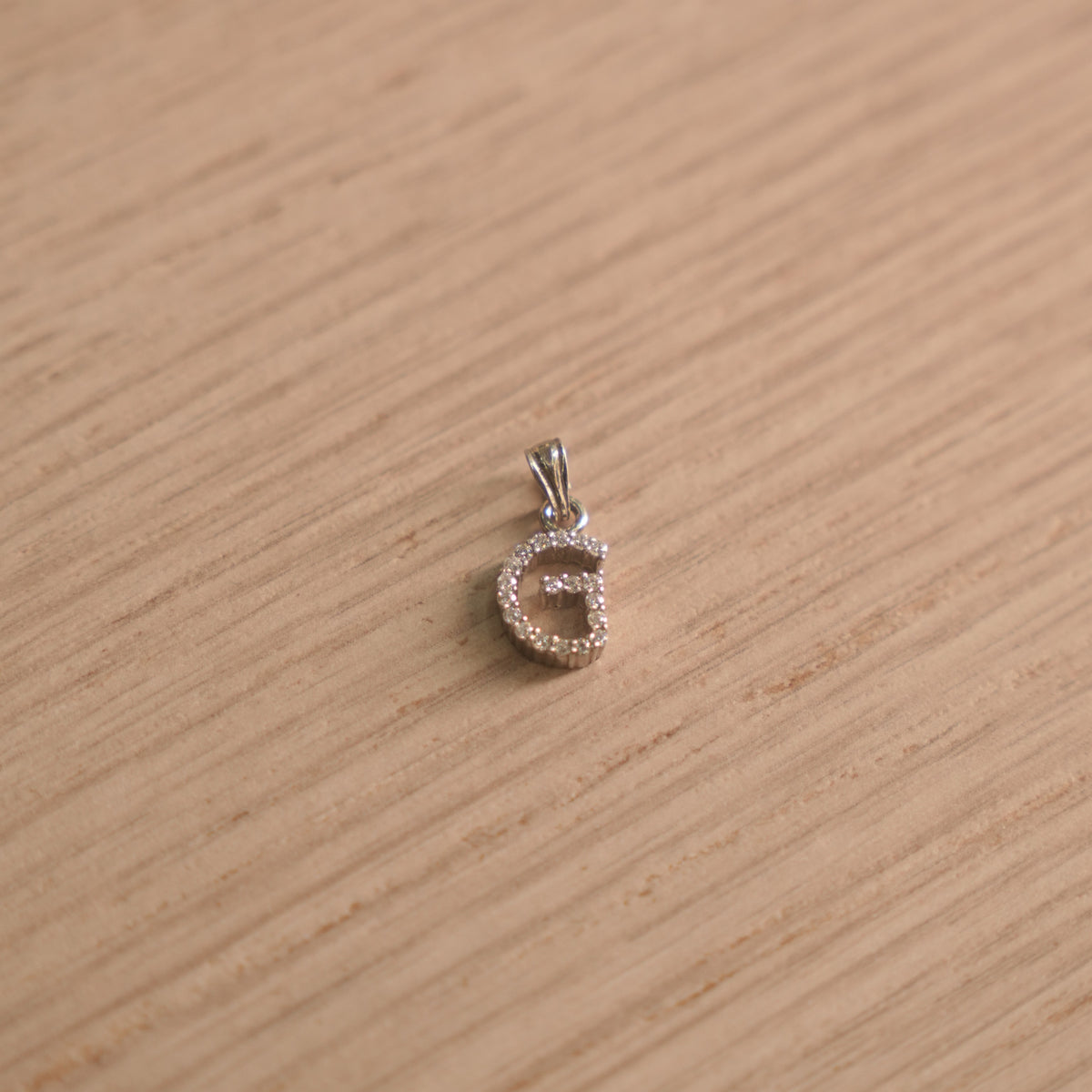Sterling silver initial G pendant pave set with American Diamond, shown with its bail on a plain background.