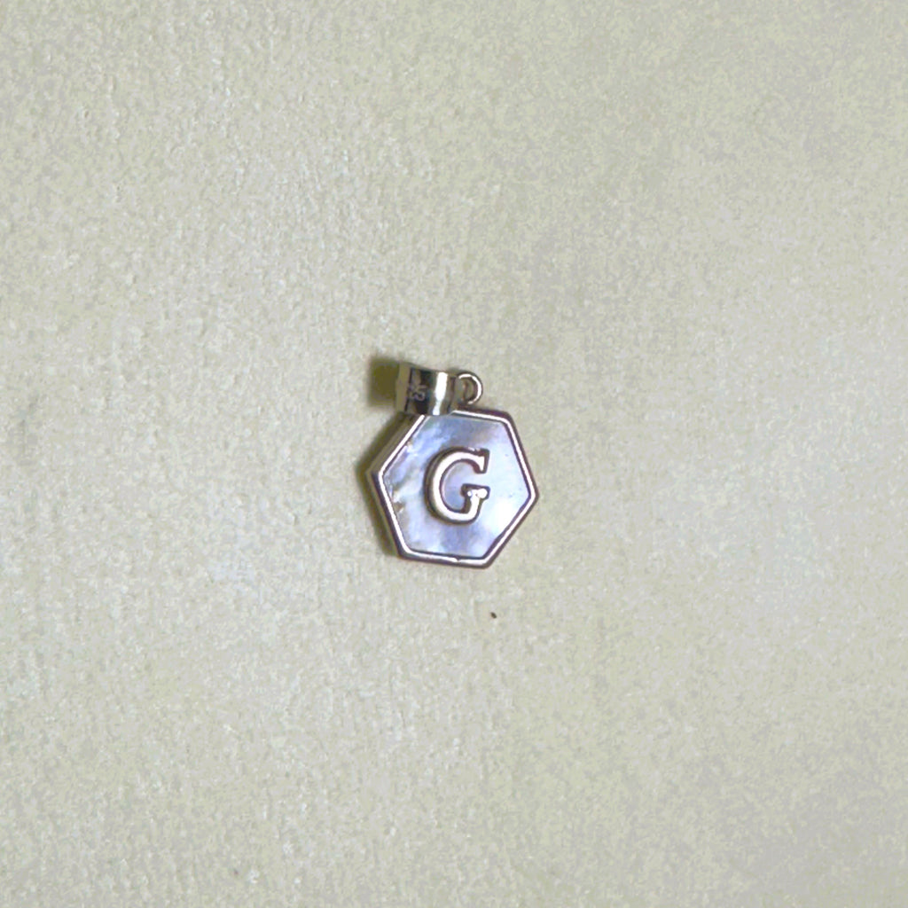 The letter G hexagon pendant on a pale surface.