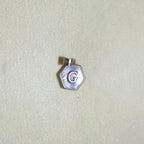 The letter G hexagon pendant on a pale surface.