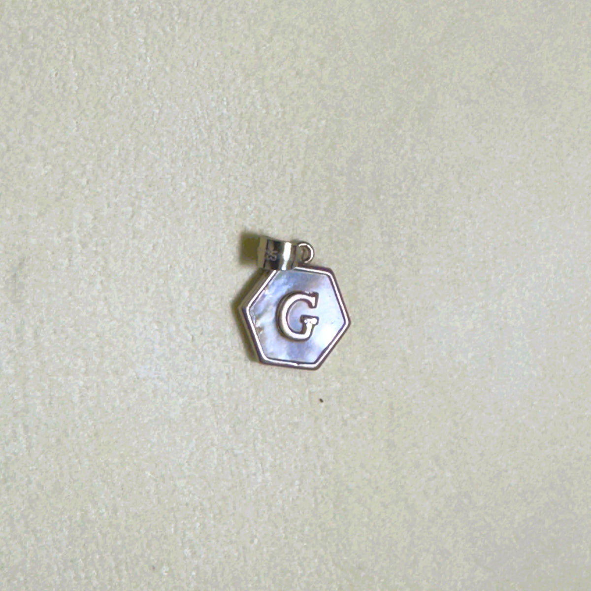 The letter G hexagon pendant on a pale surface.