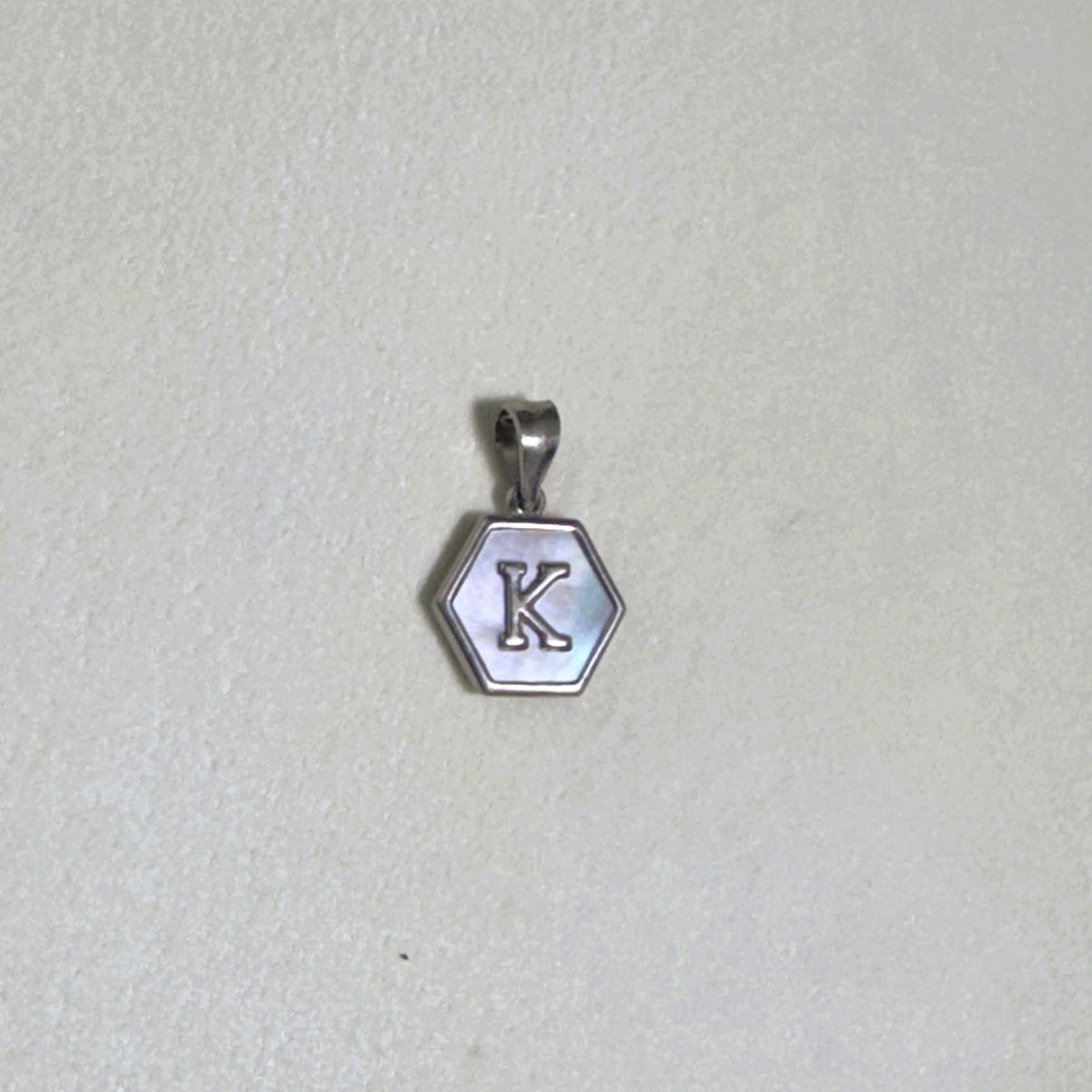 The letter K hexagon pendant on a pale surface.