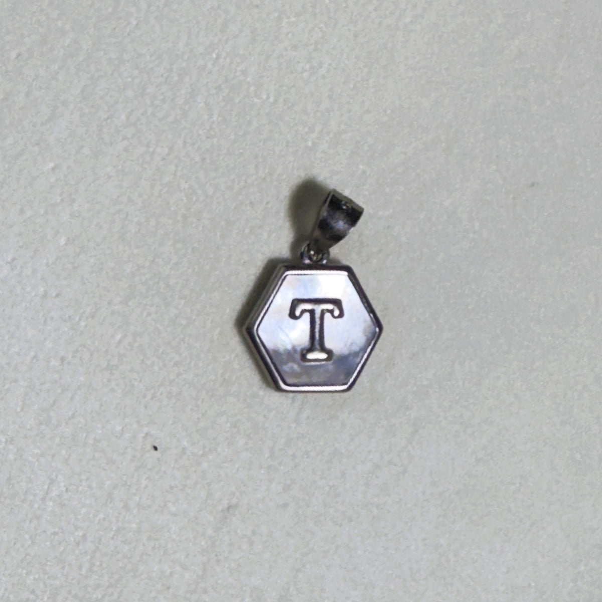 The letter T hexagon pendant on a pale surface.