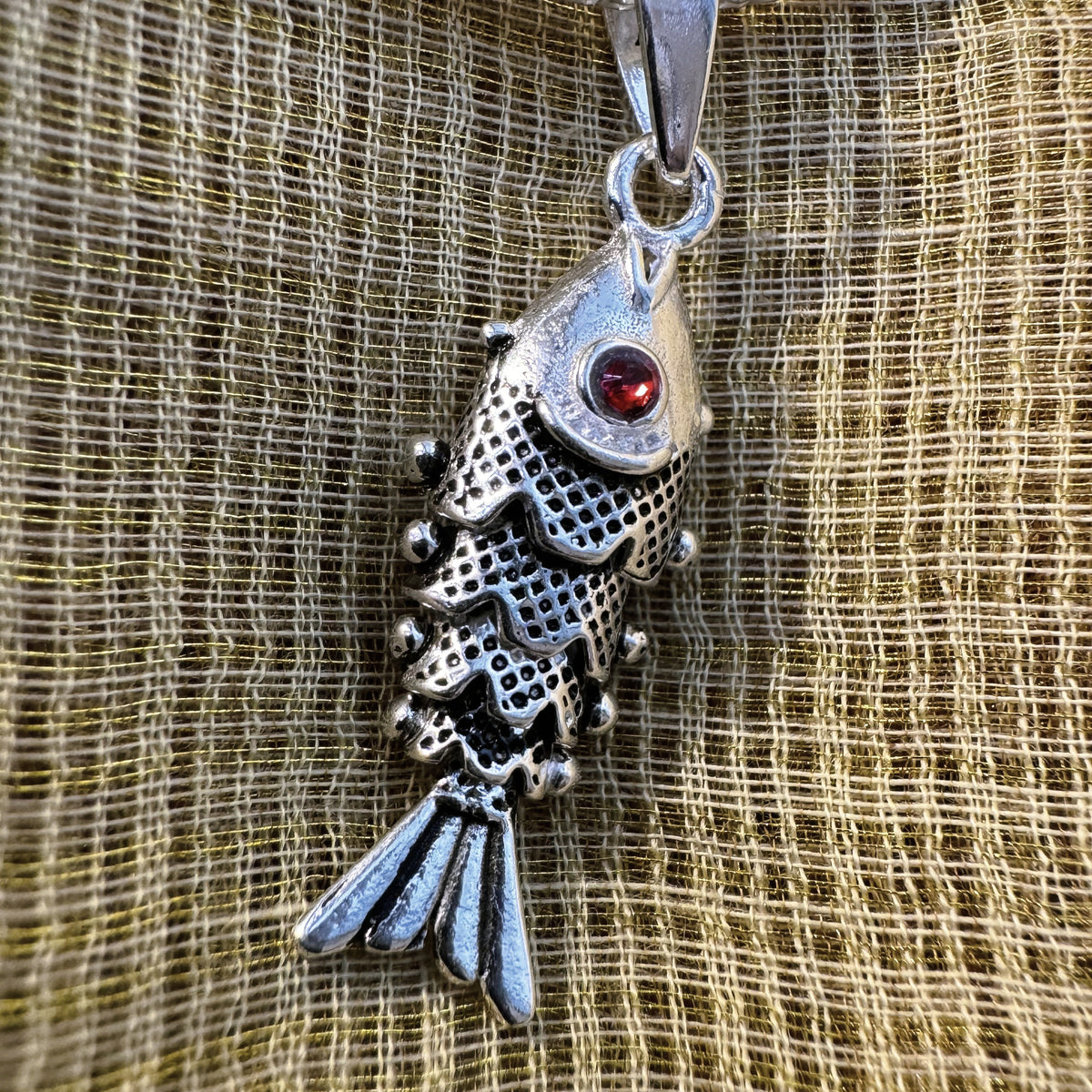 The oxidised silver fish pendant on green fabric, showing the darkened scales and bead edges.