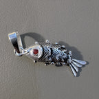 The jointed silver fish pendant lying on a grey surface with its bail to the left.