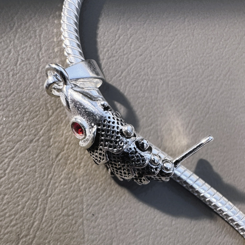 The fish pendant threaded on a silver snake chain, lying on a grey surface.