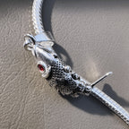 The fish pendant threaded on a silver snake chain, lying on a grey surface.