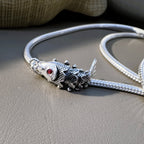 The silver fish pendant and chain lying together on a grey surface.