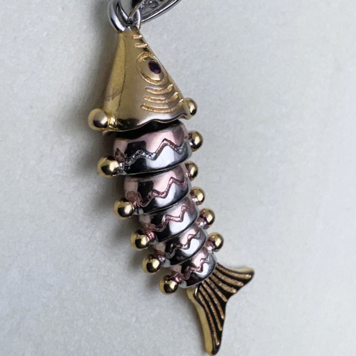 The tri-tone fish pendant seen from the side, showing the jointed segments and the red stone eye.