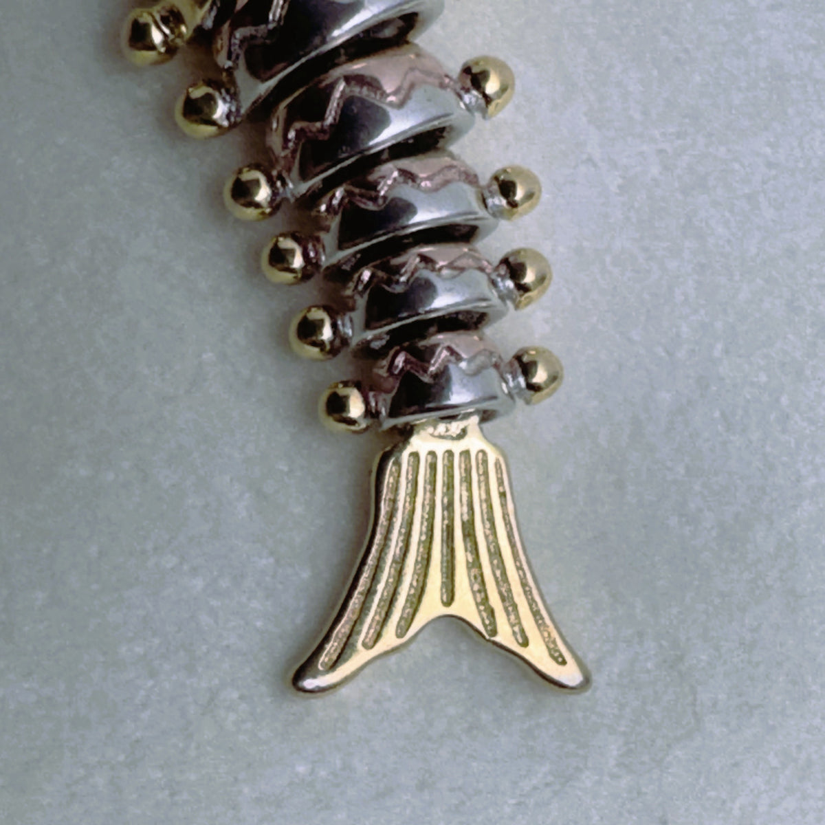 Close view of the gold-tone tail and the rose-tone and silver segments of the fish.