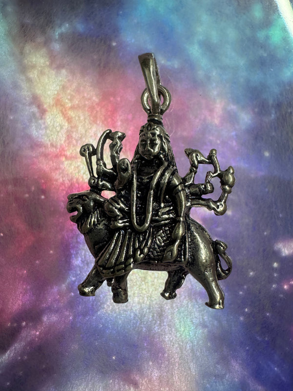 Oxidised sterling silver Goddess Durga pendant seated on her lion, against an iridescent nebula-print backdrop.