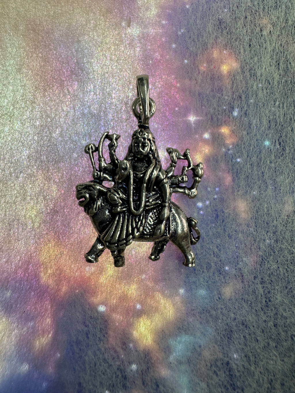 Oxidised sterling silver Durga and lion pendant lit from above on a violet iridescent background.