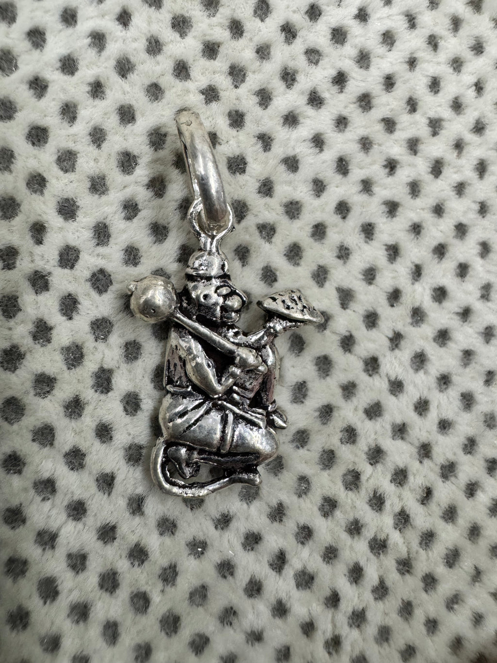 Oxidised sterling silver Hanuman pendant holding a gada and a mountain, on white fabric with grey dots.