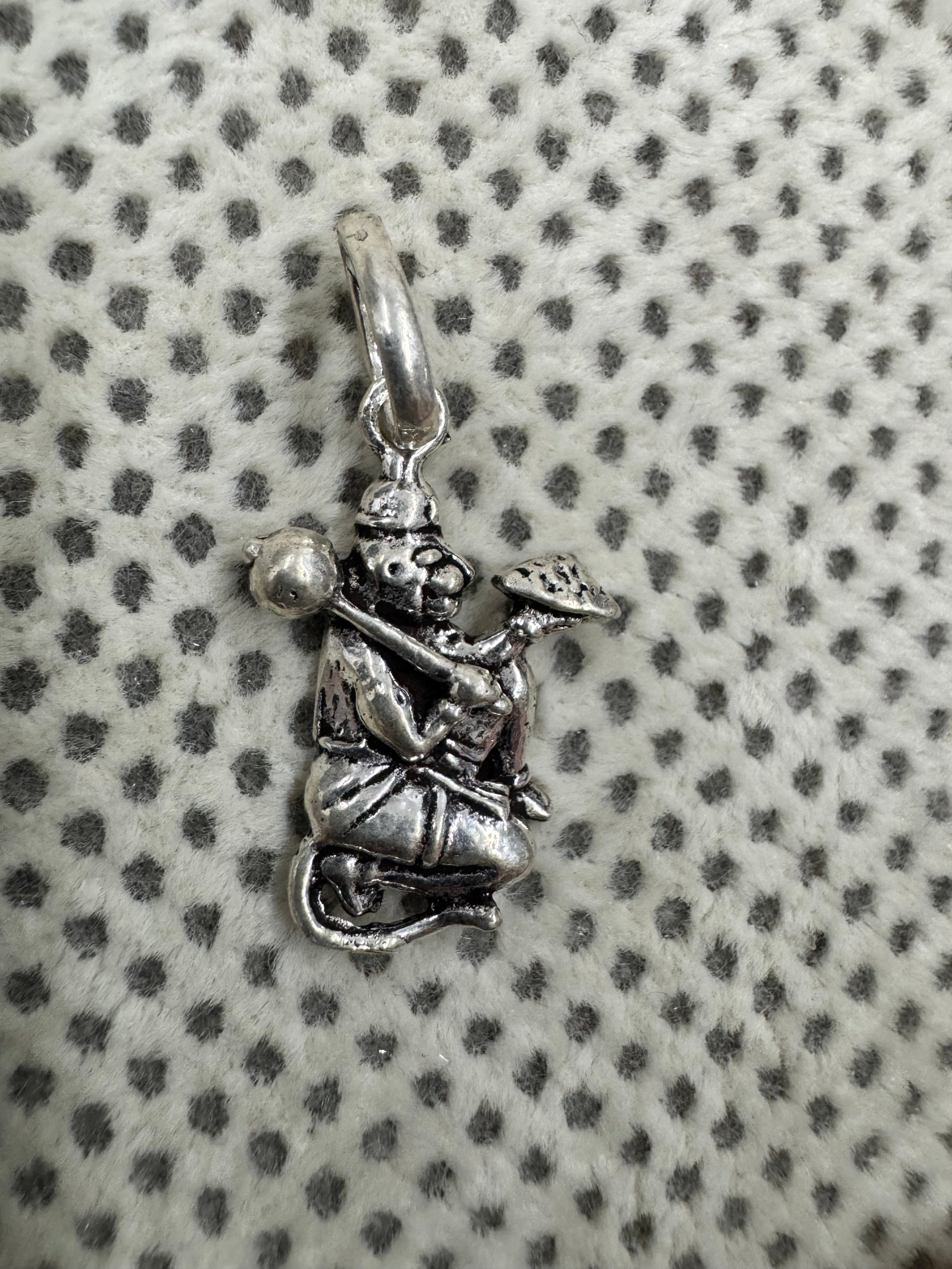 Oxidised sterling silver Hanuman pendant holding a gada and a mountain, on white fabric with grey dots.
