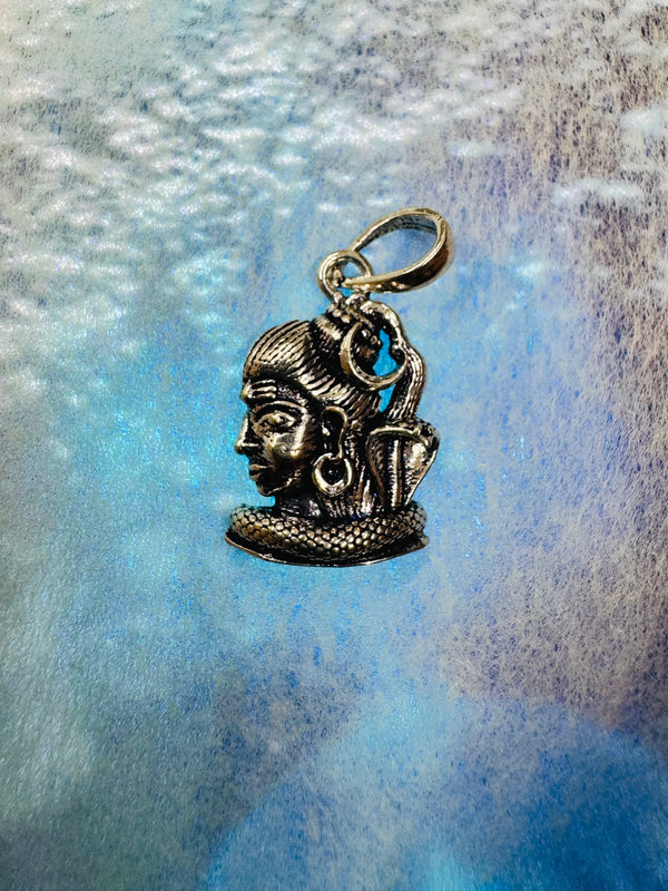Oxidised sterling silver Shiva pendant in profile with knotted hair and a cobra, on a blue iridescent background.