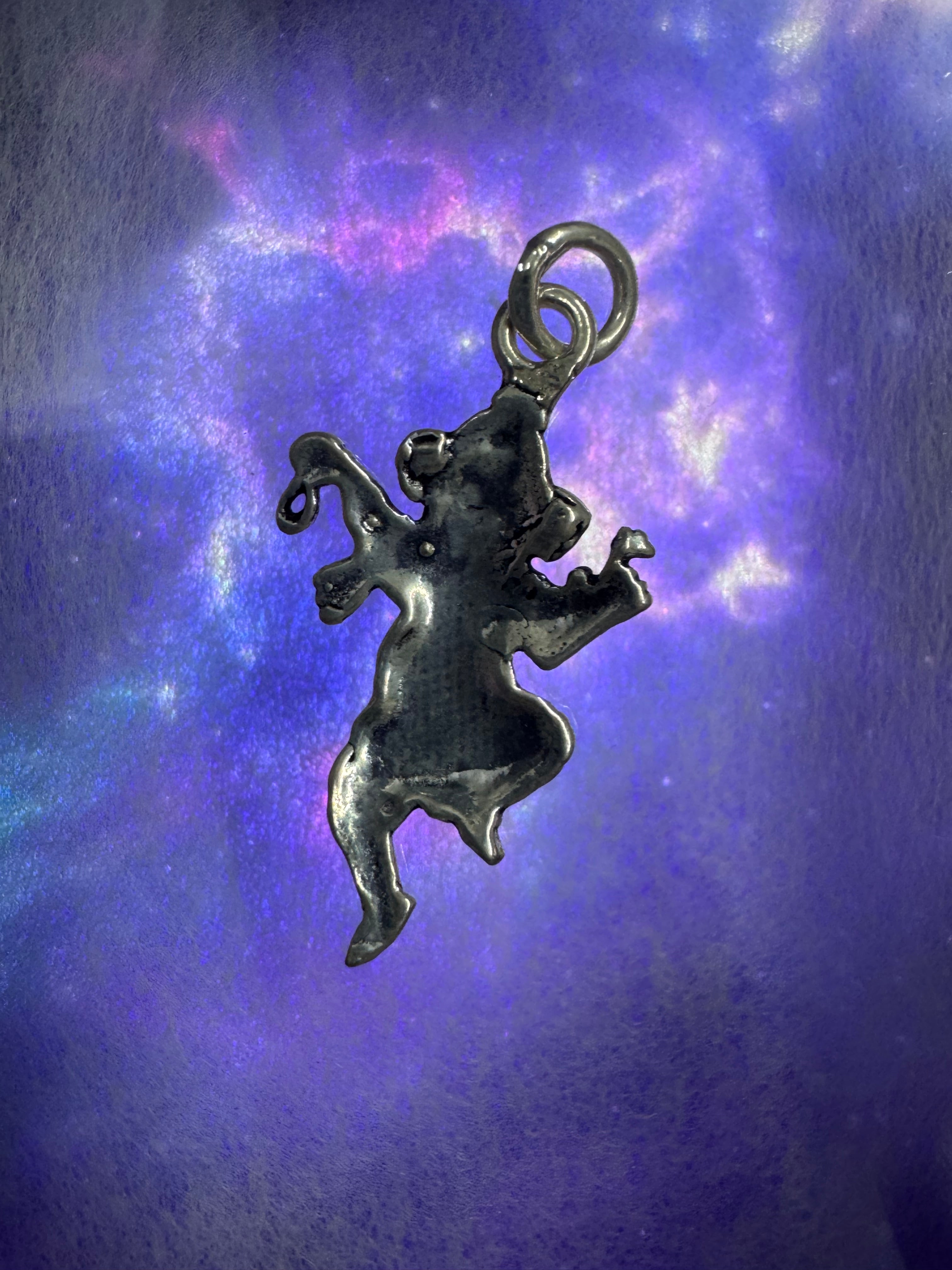 Sterling silver Ganesha pendant against a deep blue backdrop, the lifted knee, four arms and wide ears reading as a silhouette.