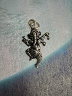 Sterling silver Ganesha pendant seen from above on pale blue-grey fabric, showing the ribbed trunk, the star-punched dhoti and the round jump ring.