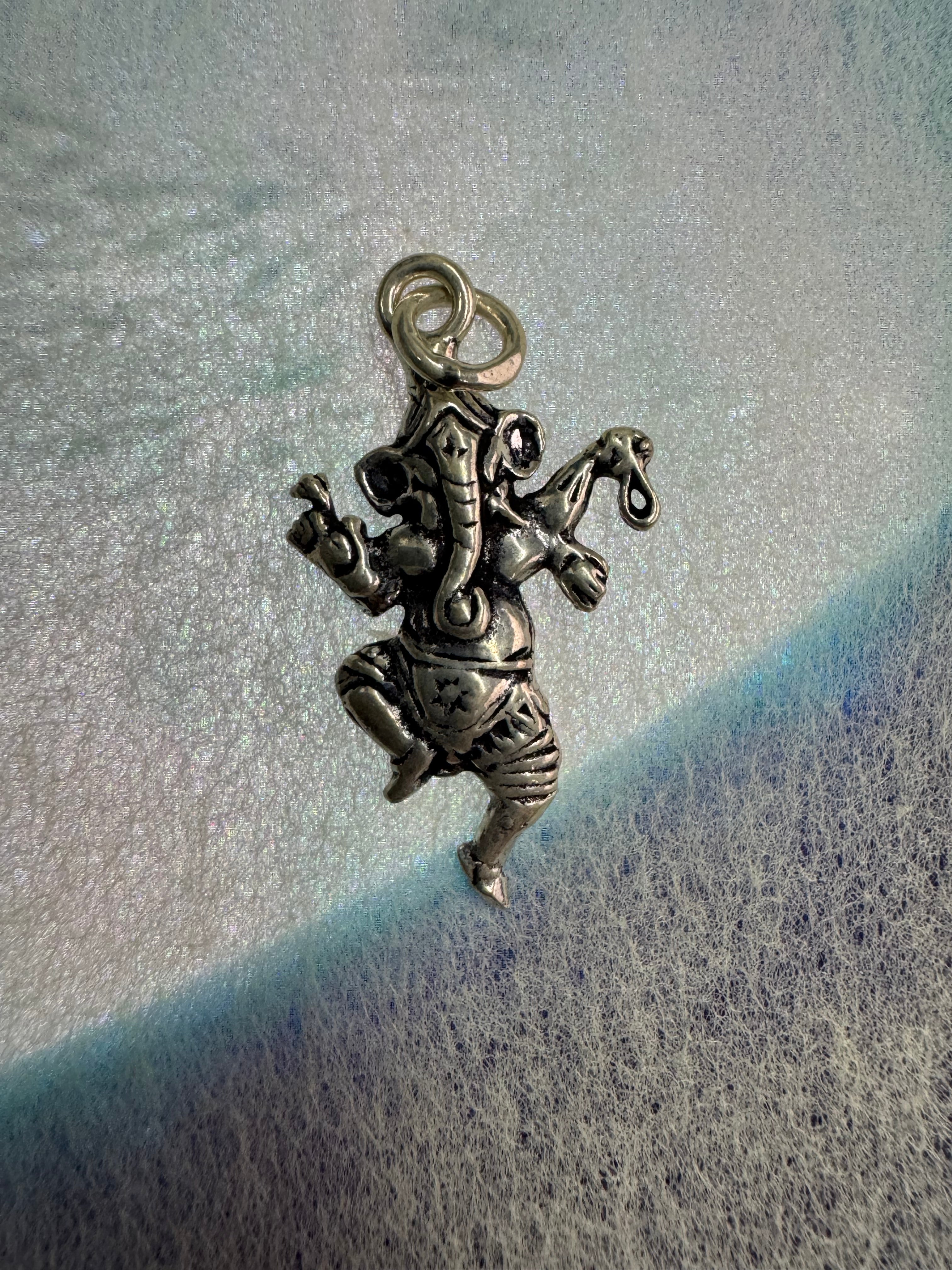 Sterling silver Ganesha pendant seen from above on pale blue-grey fabric, showing the ribbed trunk, the star-punched dhoti and the round jump ring.