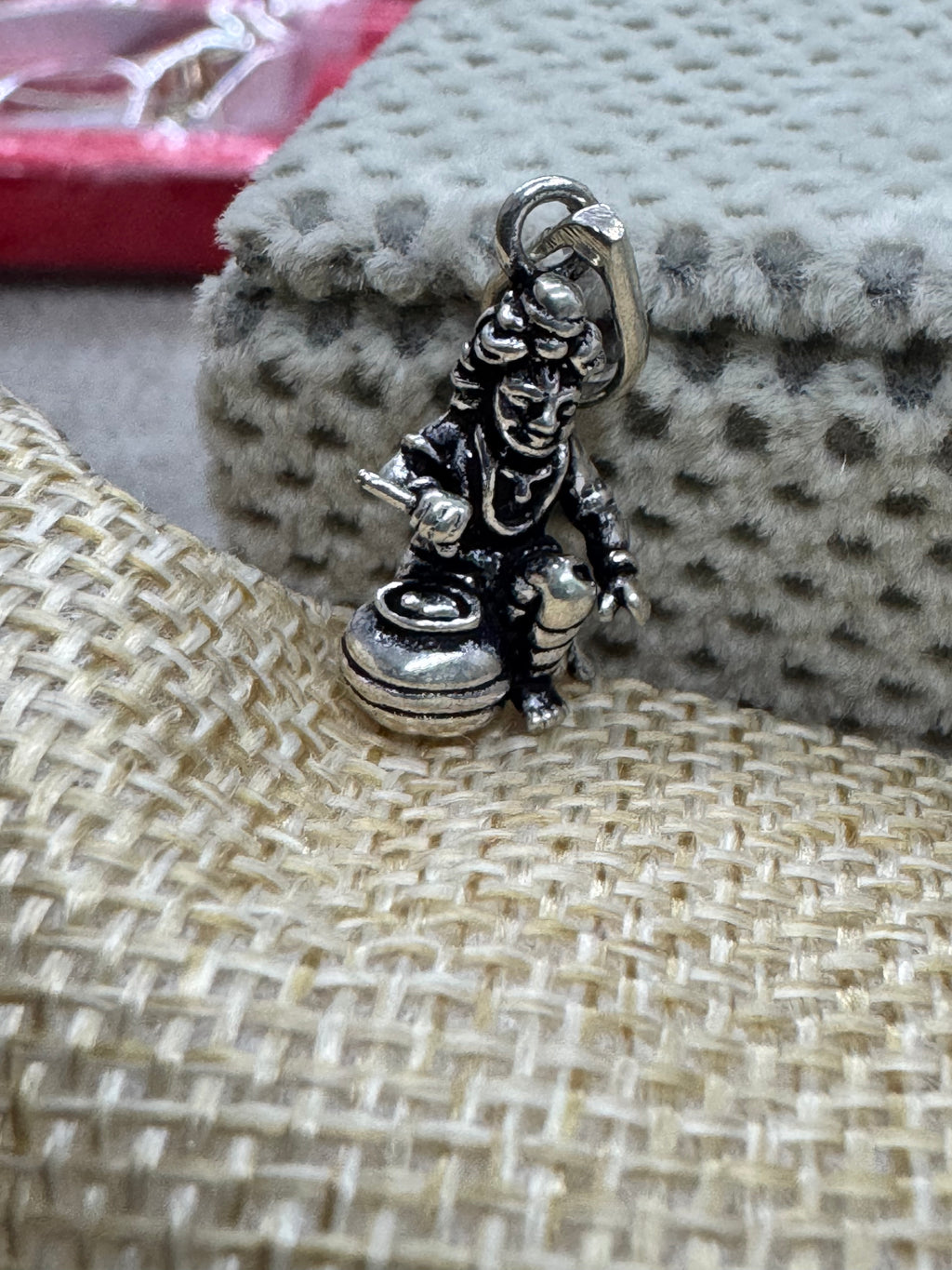 Oxidised sterling silver Bal Gopal pendant resting where grey dotted velvet meets coarse beige jute.