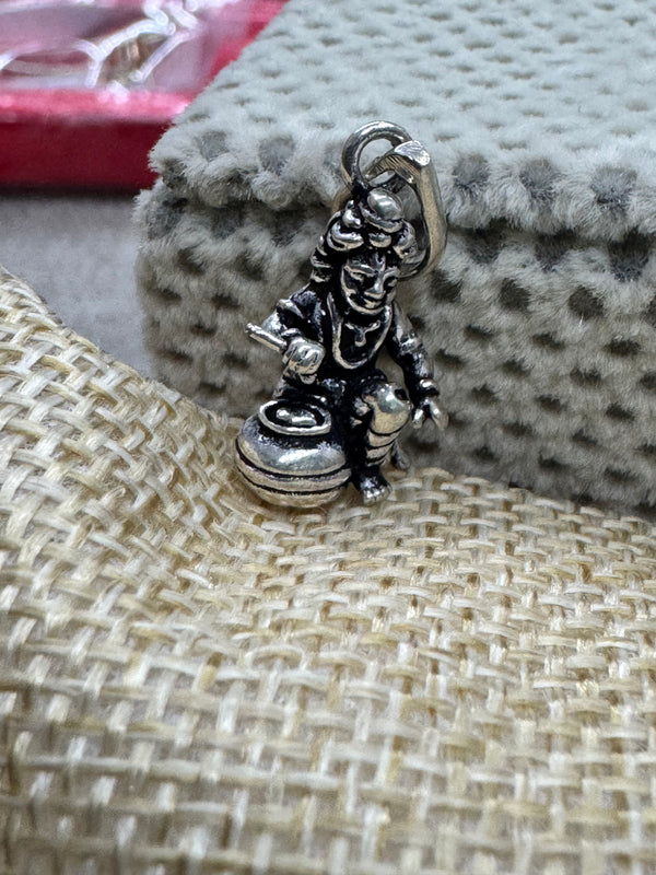 Oxidised sterling silver Bal Gopal pendant resting where grey dotted velvet meets coarse beige jute.