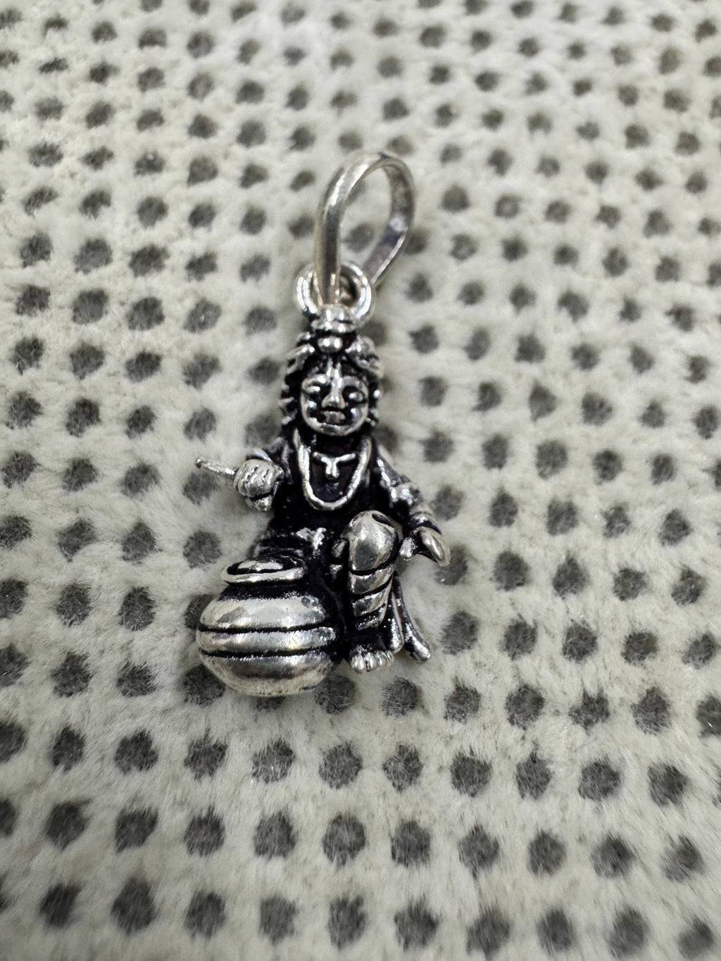 Front view of the sterling silver pendant, showing the seated figure, the raised open hand and the wide-mouthed butter pot.