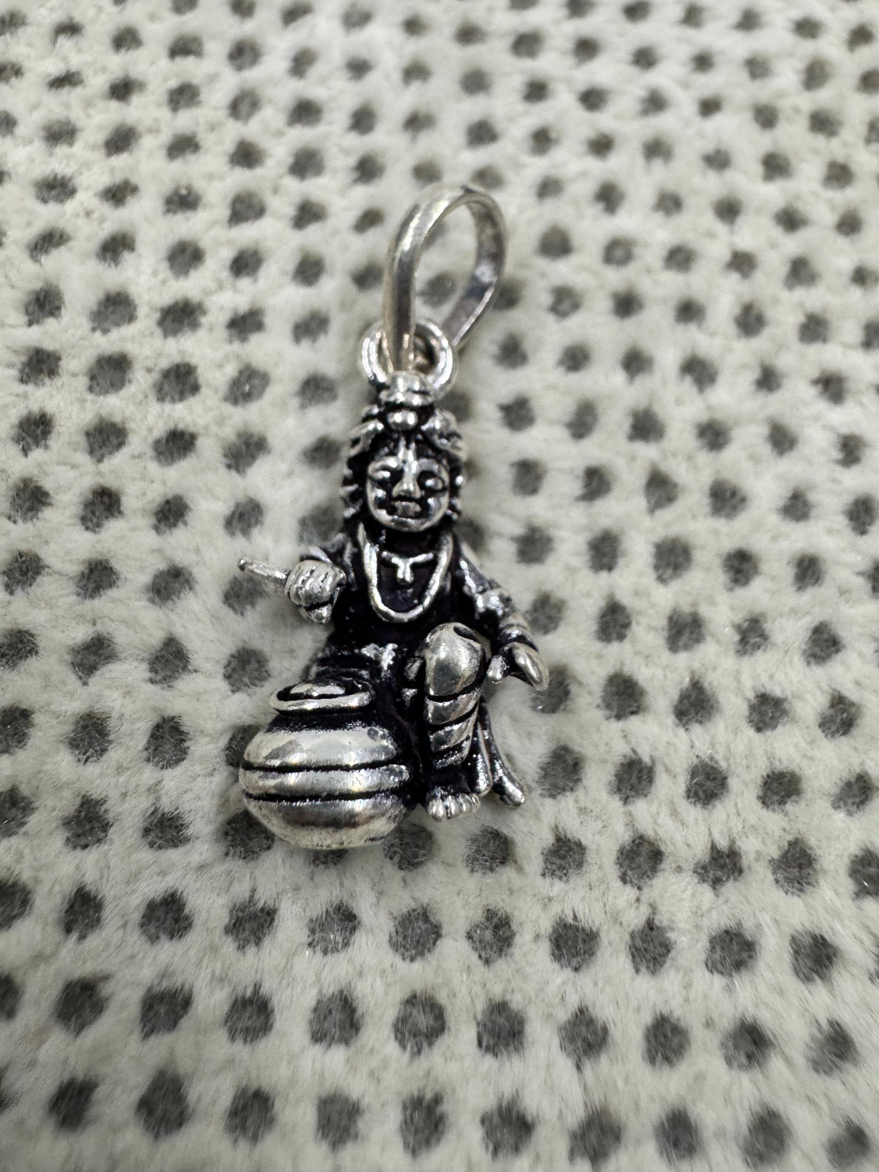 Front view of the sterling silver pendant, showing the seated figure, the raised open hand and the wide-mouthed butter pot.