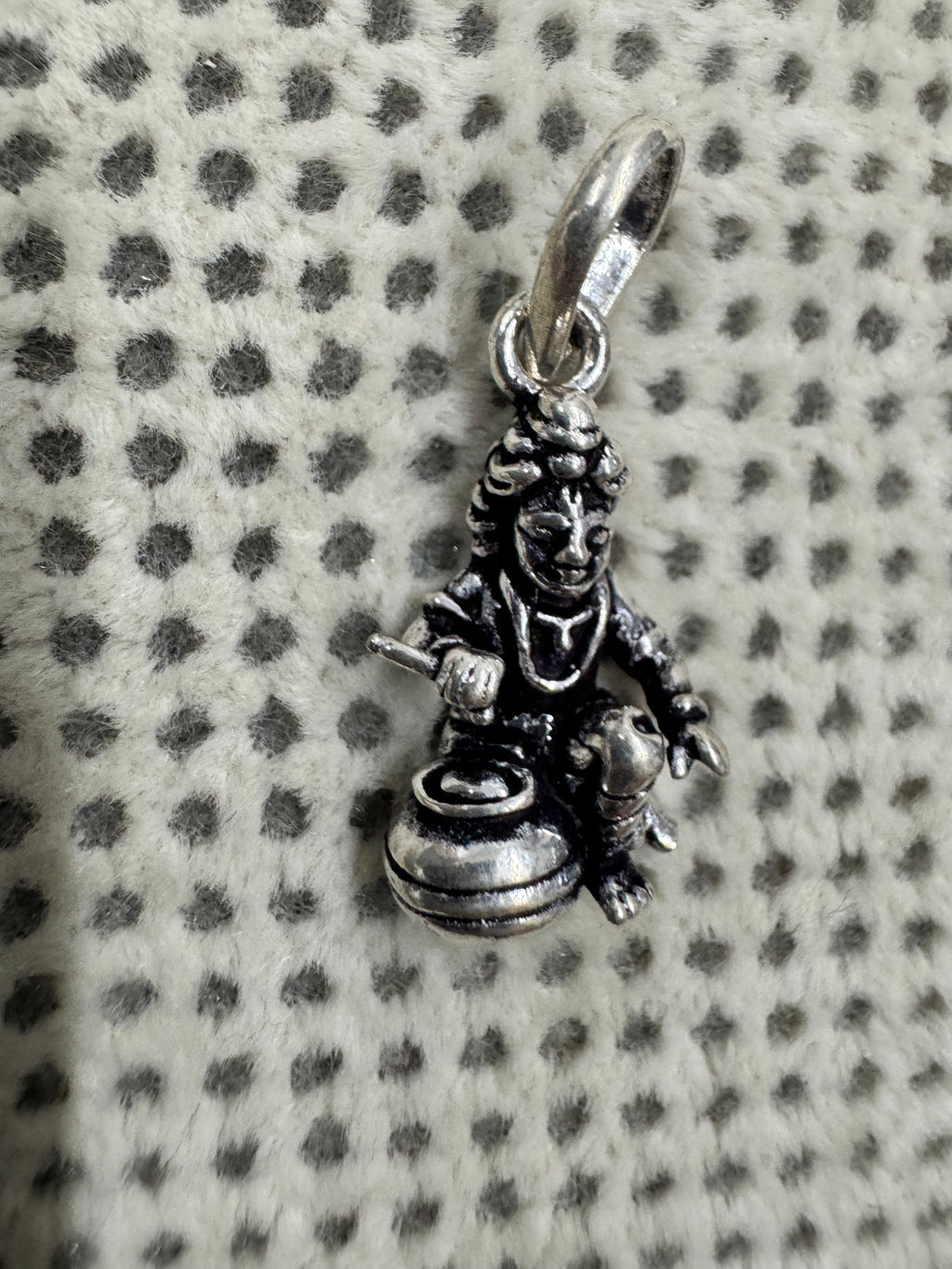 Angled view of the cast sterling silver pendant, with a short rod held above the open mouth of the butter pot.
