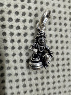 Angled view of the cast sterling silver pendant, with a short rod held above the open mouth of the butter pot.