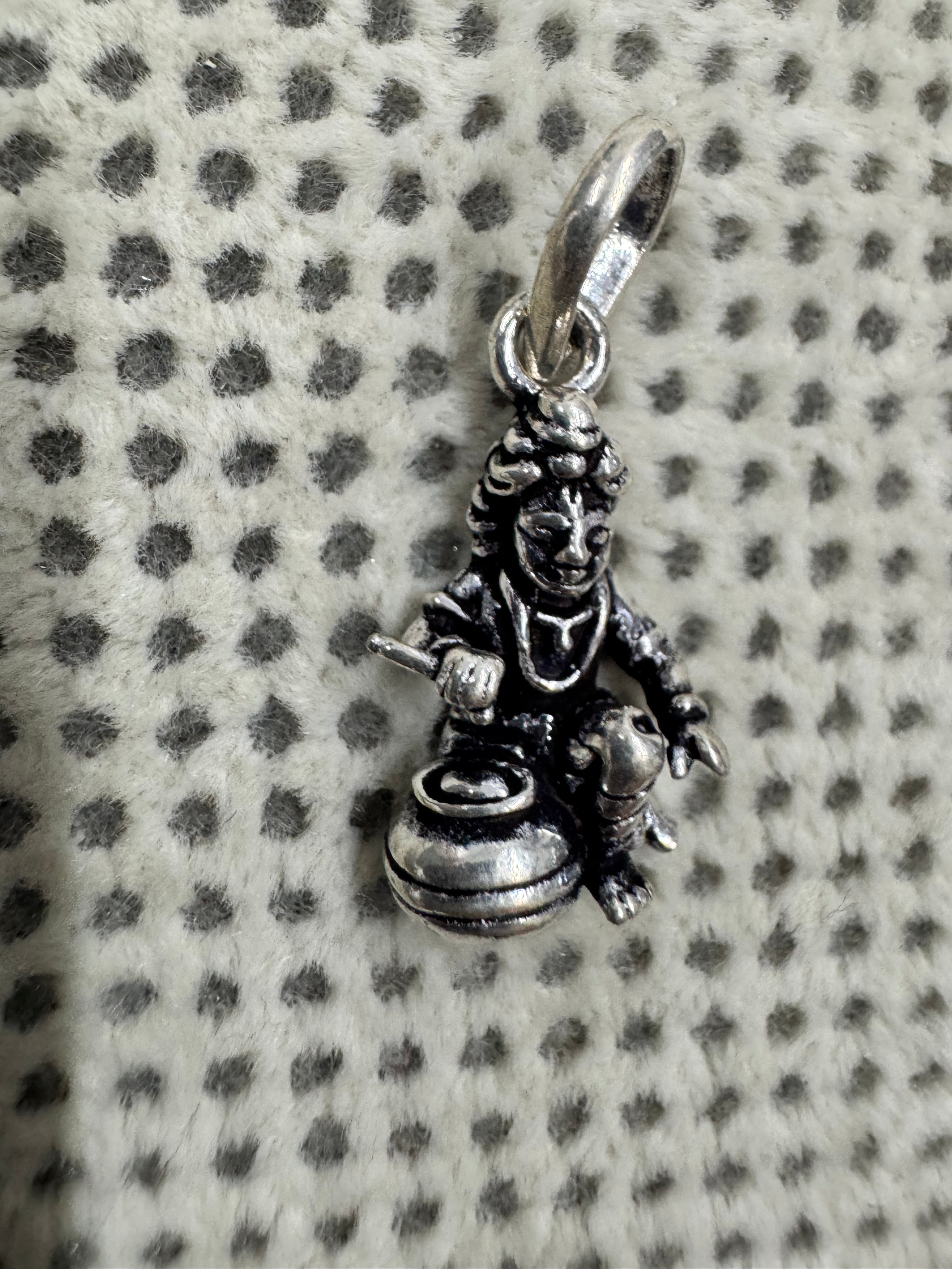 Angled view of the cast sterling silver pendant, with a short rod held above the open mouth of the butter pot.
